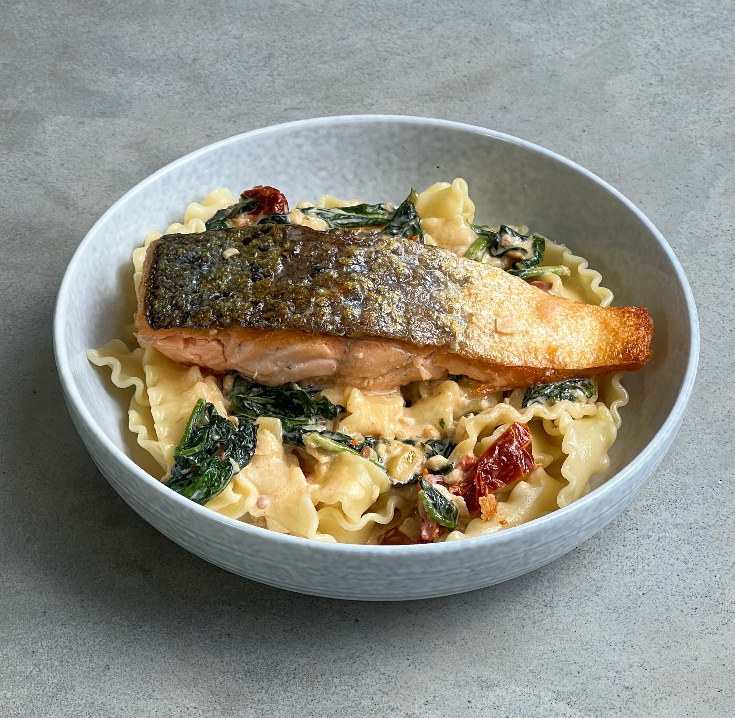 Gebakken zalm met Mafaldine pasta in een romige witte wijnsaus met vers spinazieblad en zongedroogde tomaatjes